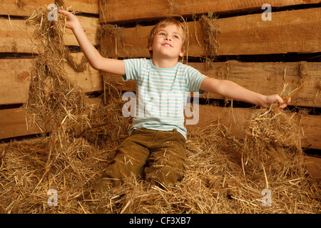 Ritratto di ragazzo giocando in mucchio di paglia nel fienile. Formato orizzontale. Foto Stock