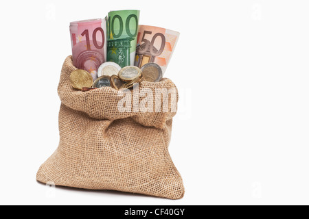 Viele Euro Banknoten und Münzen befinden sich in einem Jutesack. | molti Euro di banconote e monete in un sacco di iuta, sfondo bianco Foto Stock