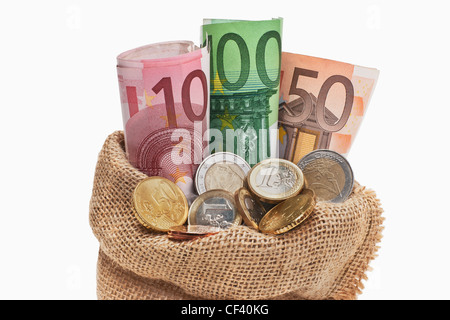 Viele Euro Banknoten und Münzen befinden sich in einem Jutesack. | molti Euro di banconote e monete in un sacco di iuta, sfondo bianco Foto Stock