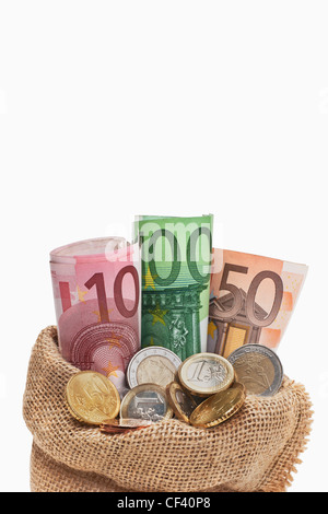 Viele Euro Banknoten und Münzen befinden sich in einem Jutesack. | molti Euro di banconote e monete in un sacco di iuta, sfondo bianco Foto Stock