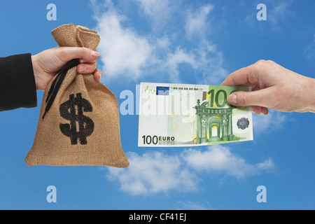 Un Euro 100 bill è tenuto in mano. Dall'altro lato un sacco di denaro con U.S. Dollar Cambio segno è tenuto in mano. Foto Stock