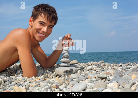 Ragazzo adolescente giacente su terreni sassosi seacoast, crea la piramide da pebble Foto Stock