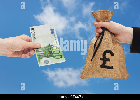 Un Euro 100 bill è tenuto in mano. Dall'altro lato un sacco di denaro con una libbra di cambio segno è tenuto in mano. Foto Stock