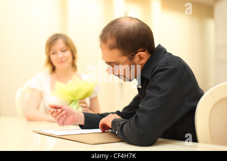 Uomo in camicia nera messa a segno su documenti di nozze, sposa sullo sfondo Foto Stock