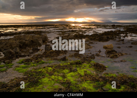 Una vista dalla riva di Culzean Bay nel South Ayrshire. L'isola di Arran e Isola Santa può essere visto sotto il sole scoppiare in Foto Stock