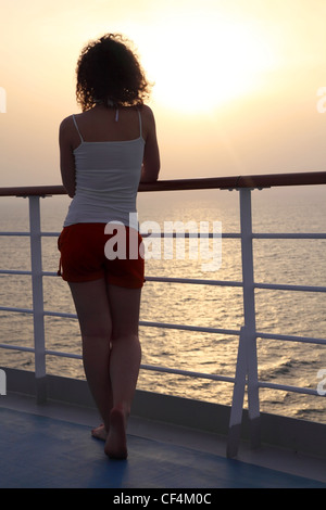 Ragazza permanente al ponte di nave e guardando in lontananza vista dal retro corpo pieno Foto Stock