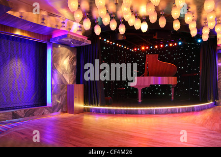 Un pianoforte sul palco vuoto con pavimento di legno e arredamento molte lampade Foto Stock