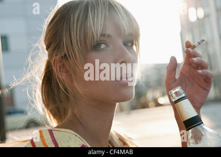 Germania, Colonia, giovane donna azienda bottiglia di birra e di fumare Foto Stock