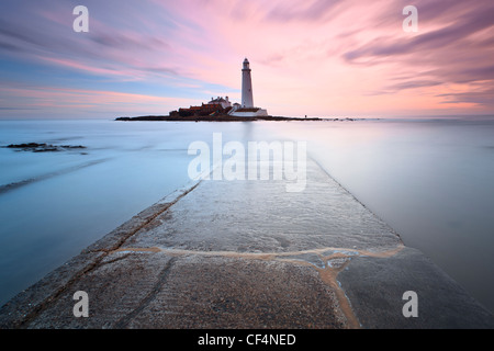 Vista lungo la parte sommersa causeway concrete che portano a St Mary's Lighthouse vicino a Whitley Bay a sunrise. Foto Stock