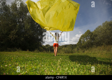 Giovane donna nella soleggiata giornata estiva tiene in mano lo sviluppo su un vento di un tessuto di colore giallo Foto Stock