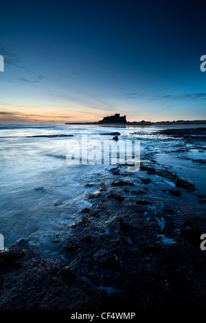 Vista lungo la costa all'alba verso il castello di Bamburgh, ex casa del re di Northumbria. Foto Stock