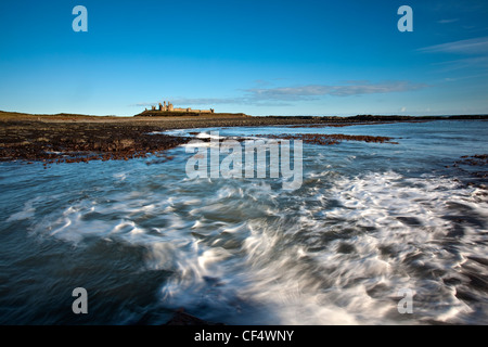 I resti del castello di Dunstanburgh costruito su di un promontorio che domina una spettacolare parte della costa di Northumberland. Foto Stock