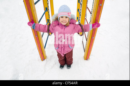 Poco abbastanza sorridente ragazza in camicia rosa sul parco giochi in inverno, ragazza messo le mani ai lati Foto Stock