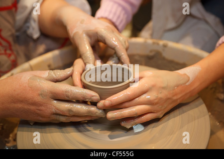 Le mani di due persone creare vaso sul tornio del vasaio. Insegnamento mestieri tradizionali. Focus sulle mani. Foto Stock