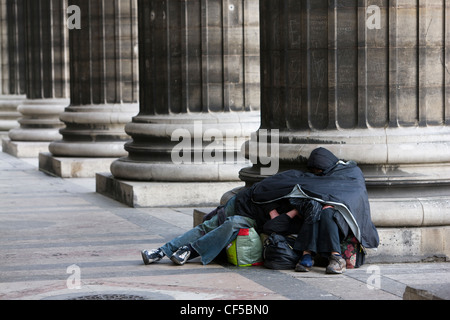 Due persone senzatetto huddle contro il freddo nei colonnati del Eglise de la Madeleine a Parigi Foto Stock