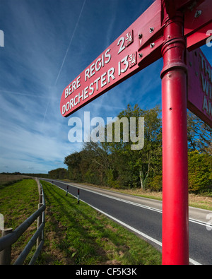 Rosso brillante cartello stradale che mostra la distanza e la direzione di bere Regis e Dorchester. Foto Stock