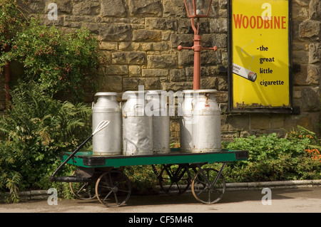 Bidoni per il latte e il carrello sulla piattaforma alla stazione di Goathland davanti a un vecchio Woodbine annuncio di sigaretta. Foto Stock