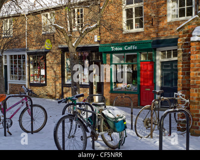 Biciclette bloccato per rastrelliere nella neve al di fuori di una fila di negozi in Minster vicino. Foto Stock