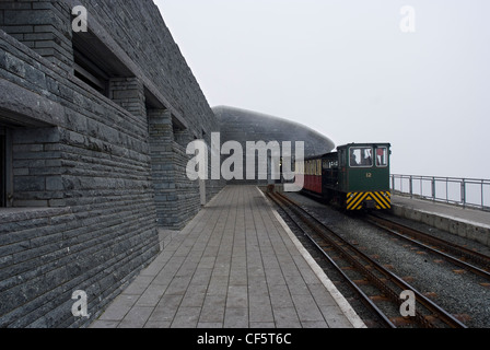 Un treno sulla ferrovia di Snowdon Mountain accanto alla piattaforma al di fuori del nuovo Snowdon centro visitatori al vertice. Foto Stock