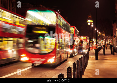 Double Decker autobus rossi di Londra che viaggiano attraverso la città di notte con il Big Ben in background. Foto Stock