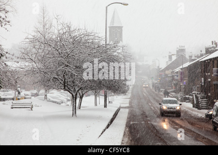 Auto percorrendo una strada attraverso un villaggio sotto la neve. Foto Stock