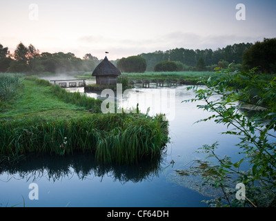 Pesca con tetto di paglia di capanna e trappole di anguilla sul fiume Test a Longstock. Foto Stock