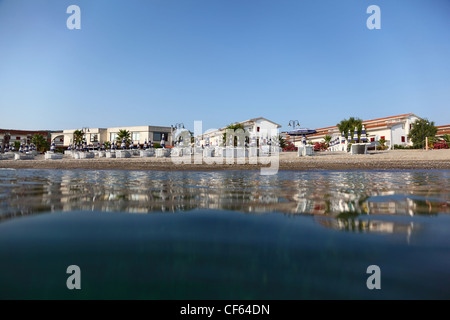 Spiaggia mare su cui sedie a sdraio sono costruiti con ombrelloni per le scottature e a due piani cottages costo Foto Stock