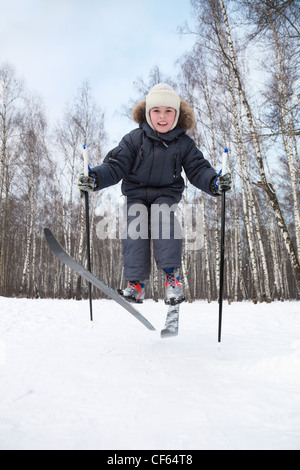 Giovane ragazzo salta su sci da fondo interno inverno foresta alla giornata di sole Foto Stock