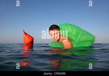 Giovane uomo nuota in mare sul verde lifeline. arancione boa di ancoraggio galleggia sul mare. Foto Stock