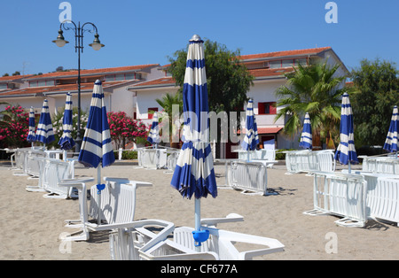 Molti con strisce bianche sedie a sdraio e ombrelloni sono sulla spiaggia vuota. Foto Stock