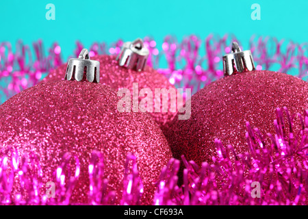 In alto di tre rossi albero di Natale sfere circondato da viola tinsel isolato sul blu, sfera di sinistra nel fuoco. Foto Stock