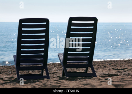 In plastica due sedie vuote riposare sulla spiaggia vicino al mare di fronte sun Foto Stock