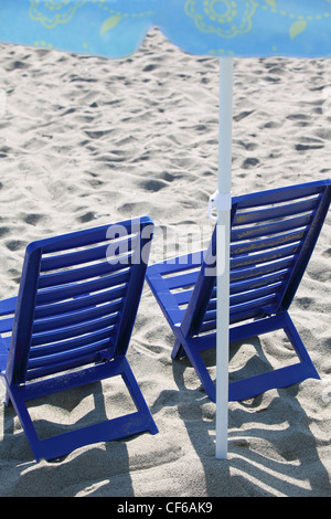 Due blu scuro sedie in plastica stare sulla spiaggia sotto ombrellone Foto Stock