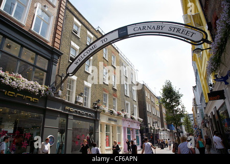 Gli amanti dello shopping passando sotto il segno di ingresso a Carnaby Street a Londra. Foto Stock