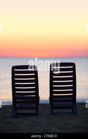 Due sedie vuote stand sulla sabbia vicino al mare durante il tramonto Foto Stock