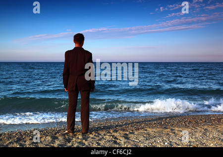 Nudi uomo in tuta sta torna su pietra costa alla sera Foto Stock