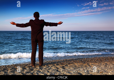 Nudi uomo in tuta sta indietro e aprire le mani su pietra costa alla sera Foto Stock