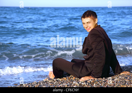 Nudi uomo sorridente in tuta siede sulla costa di pietra a sera Foto Stock
