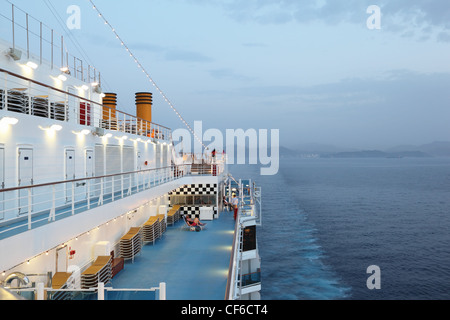 Grande nave da crociera di equitazione in serata. luce su. Alcune delle persone sul ponte della nave da crociera Foto Stock