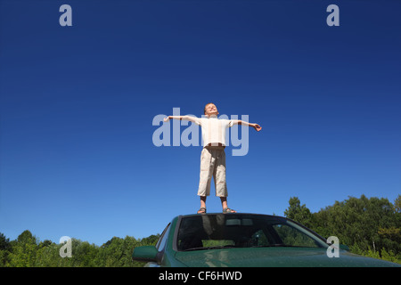 Bambino si alza sulla testa di auto, ascensori faccia in cielo e invia le mani ai lati Foto Stock