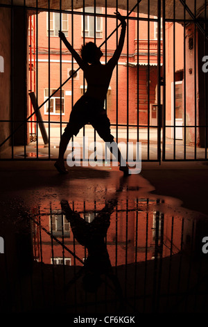 Silhouette di dancing girl nel buio, ha tenuto dietro a traliccio, stese le braccia e le gambe Foto Stock