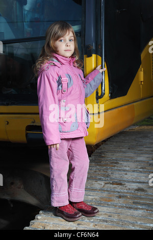 Bambina abiti rosa permanente giallo sul trattore cingolato nel buio Foto Stock