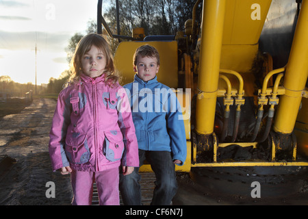 Bambina abiti rosa e il ragazzo in giacca blu in piedi vicino a giallo trattore cingolato Foto Stock