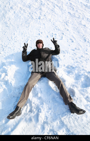 La gioventù si trova sulla neve sulla schiena e mostra il gesto delle mani di vittoria e risate Foto Stock