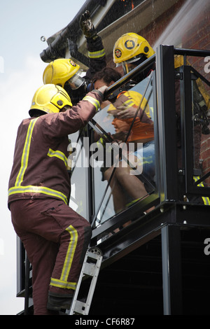 I vigili del fuoco di proteggere una donna come suo soccorso da un incendio in un blocco di appartamenti a Ilford Foto Stock