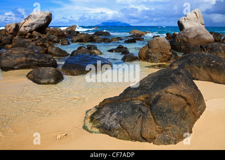 Vicino al Sunset Beach, Mahe, Seychelles che mostra il granito formazioni rocciose e Silhouette Island all'orizzonte. Foto Stock