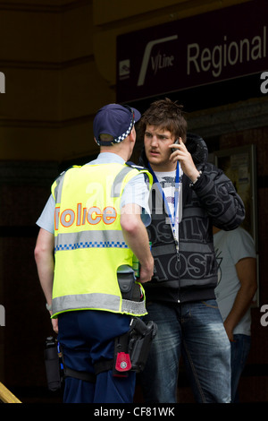 Poliziotto a parlare con i giovani sul telefono cellulare, la stazione di Flinders Street, Melbourne, Australia Foto Stock