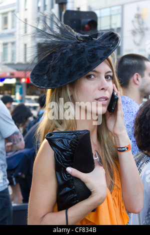 Moda Donna parlando al telefono cellulare proveniente da Melbourne corse di cavalli presso la stazione di Flinders Street, Melbourne, Australia Foto Stock