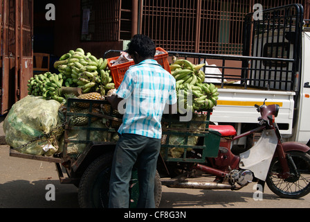 Uomo di mercato trasporto pesante carico di vegetali in piccoli risciò ciclo.Una scena dal Bazaar Chalai mercato in Kerala, India Foto Stock