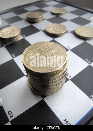 Impilate i quantitativi di British una libbra di monete di sedersi su un bianco e nero checkers , gioco di scacchi bordo. Foto Stock